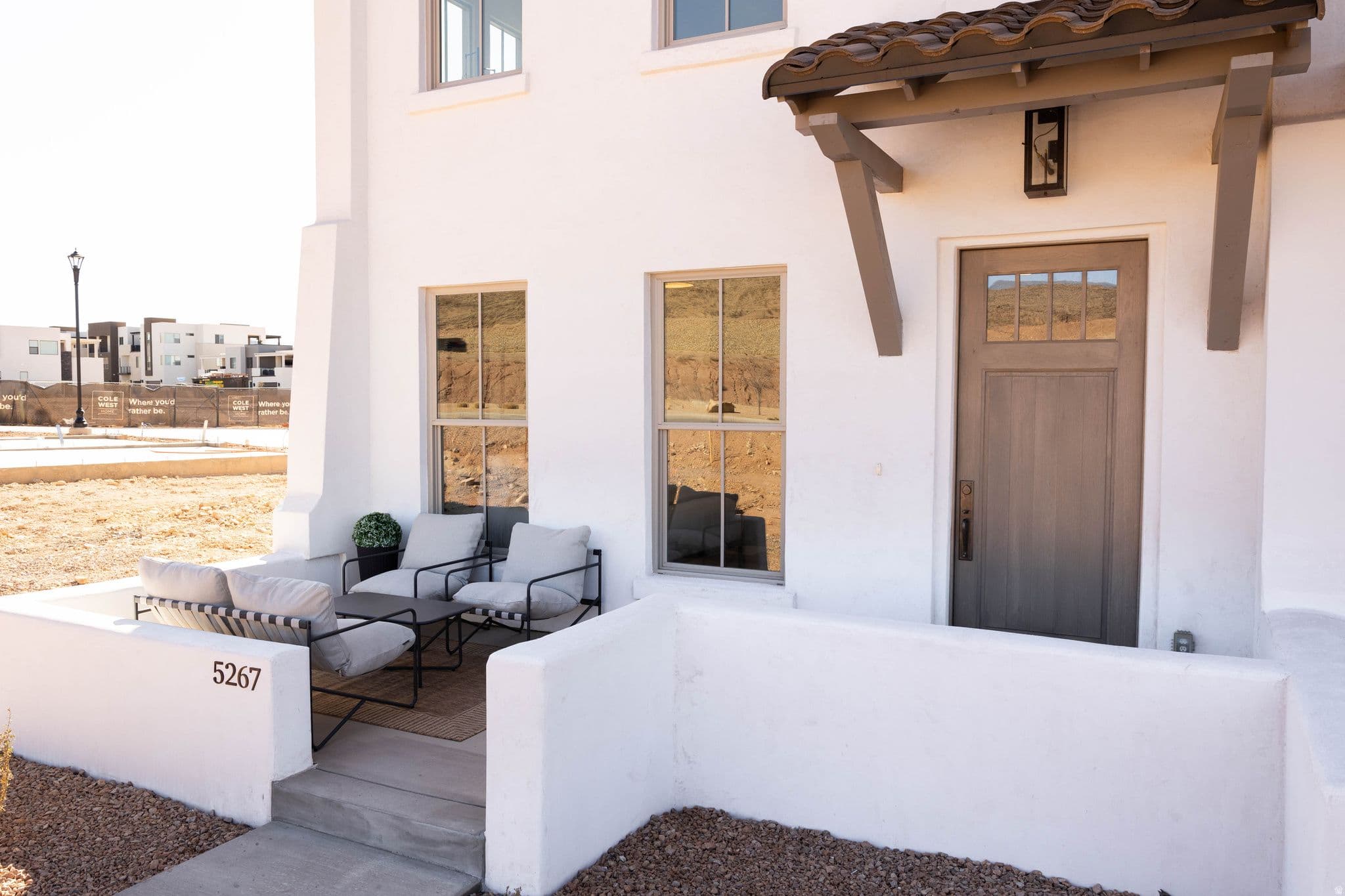 White stucco exterior featuring a covered entry, wood-finish front door with glass panes, decorative tile roof over the entry, sconce lighting, and a private front patio